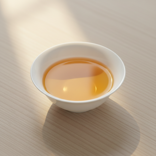 Té oolong servido en taza baja y plana de porcelana bone china, líquido ámbar dorado brillante, mesa de fresno con luz dorada